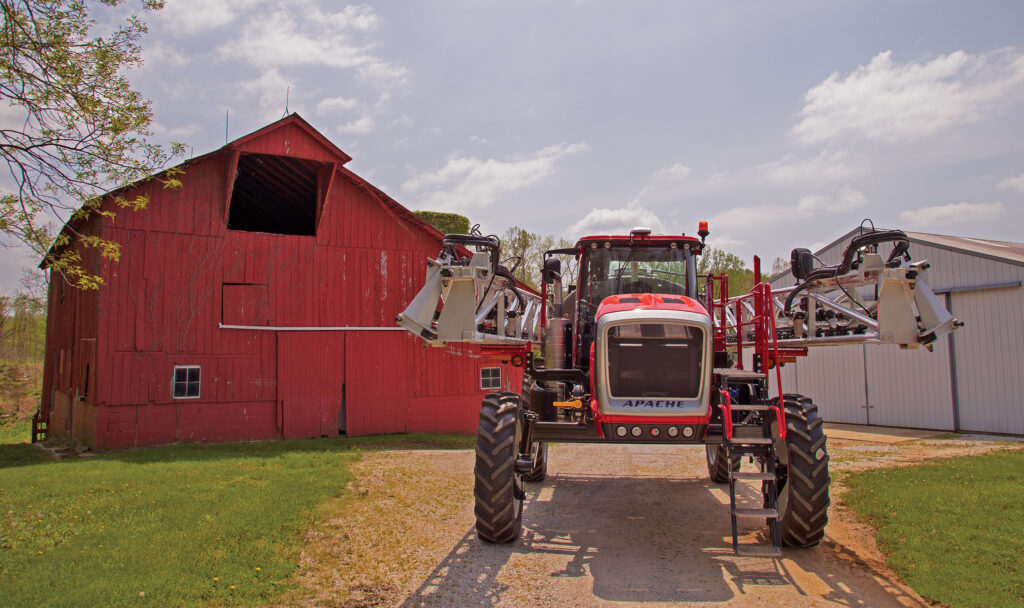 shot of the front of an apache sprayer that is located in front of a red barn